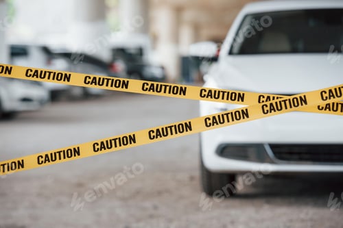 Preview: Front of modern luxury vehicle. Yellow caution tape near the car parking lot at daytime. Crime scene