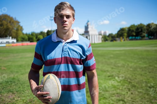 Preview: Rugby player holding ball on field, wearing striped jersey, looking determined, copy space