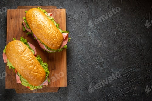 Preview: Top view of homemade sandwiches on wooden cutting boards on black distressed background