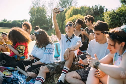 Preview: Group of friends relaxing, using smartphone in park