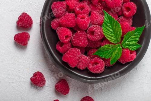 Preview: fresh raspberries, on a black plate, with leaves, top view, on a white table,