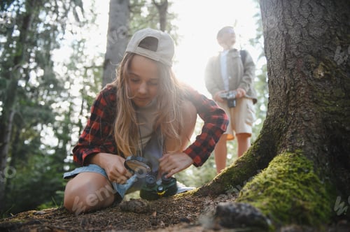 Preview: Young explorers examining nature with magnifying glass and binoculars in forest