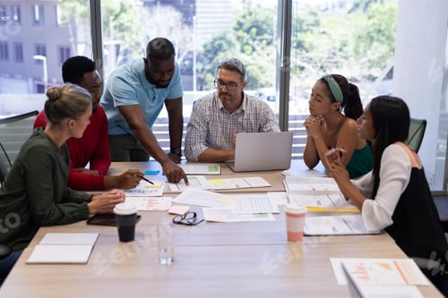 Preview: Biracial female and male advisors discussing over boardroom during meeting at modern workplace
