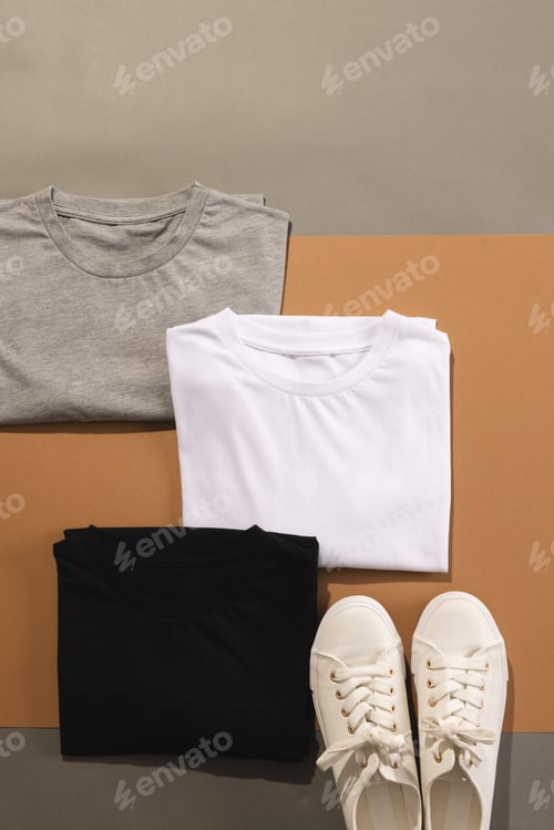 Preview: Close up of folded t shirts and white sneakers and copy space on brown background