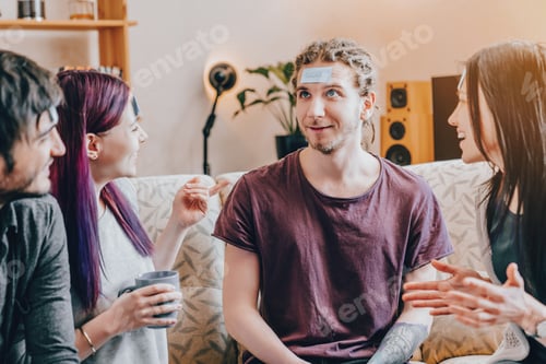 Preview: Young friends playing name guessing game at home, sitting on couch, laughing trying to guess words