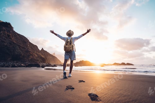 Preview: Young man arms outstretched by the sea at sunrise enjoying freedom and life