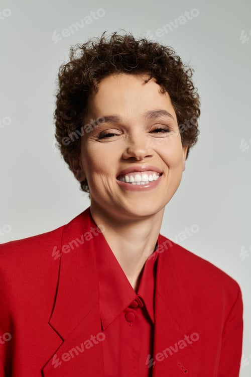 Preview: Beautiful young woman in vibrant red suit with cheerful smile against neutral background