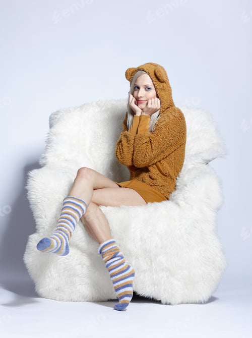 Preview: Portrait Of Beautiful Blonde Girl In Brown Plush Hud With Bear Ears Sitting On Big White Furry