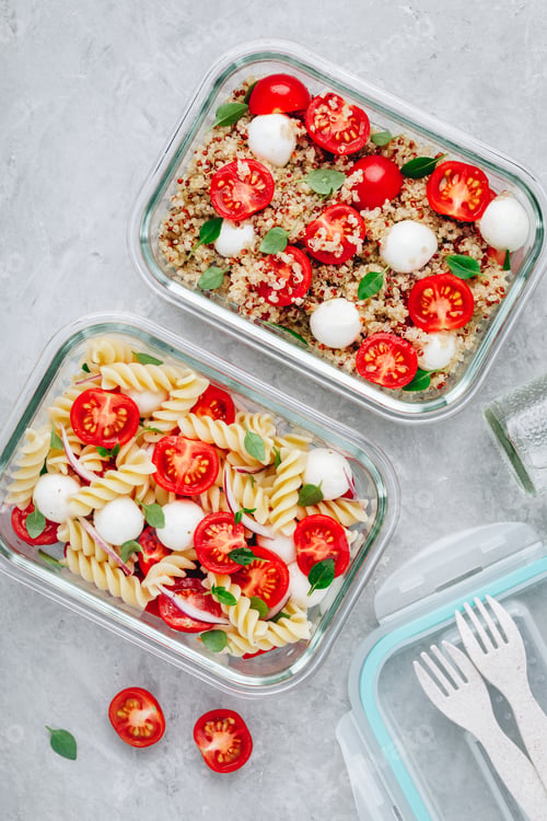 Vista previa: Meal prep containers with pasta salad or quinoa, tomatoes, mozzarella cheese, and basil.