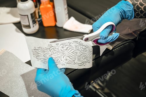Preview: Tattoo artist preparing stencil cutting the design with scissors