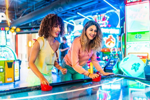 Preview: Two female friends playing air hockey in a colorful arcade