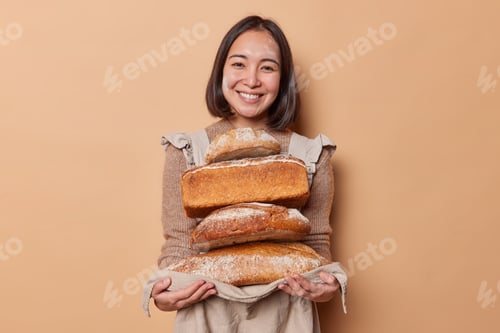 Preview: Happy Asian woman holds stack of loaves of bread on napkin demonstrates yeast free organic food