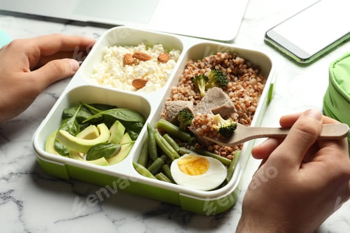 Preview: Man eating natural protein food from container at office table