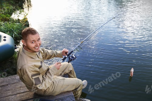 Preview: Man with rod fishing on wooden pier at riverside. Recreational activity