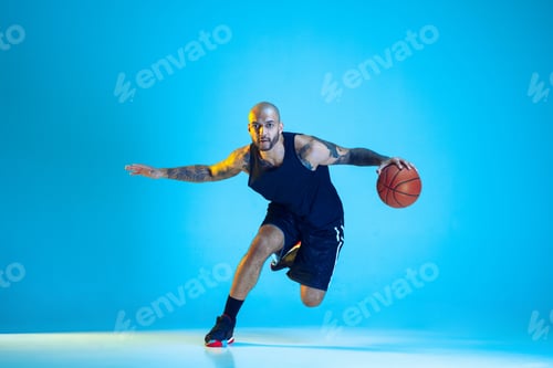 Preview: Young basketball player training isolated on blue studio background in neon light