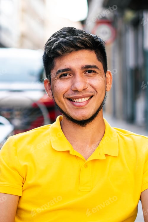 Preview: Young latin man sitting on a terrace looking at camera smiling