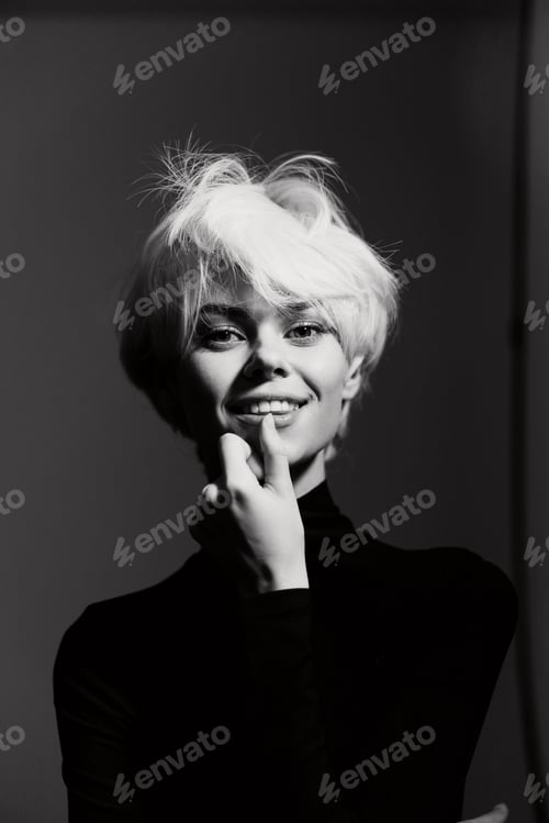 Preview: Cheerful young woman with short blonde hair in a black turtleneck, smiling playfully and touching