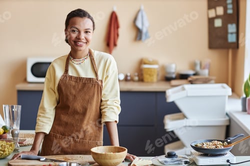 Preview: Young black woman standing in kitchen and smiling at camera cheerfully