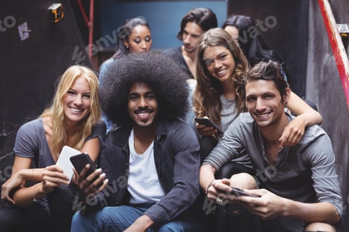 Vista previa: Retrato de amigos sonrientes usando teléfonos móviles en los escalones de la discoteca
