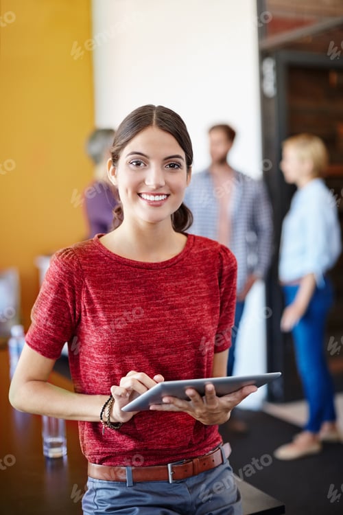 Preview: Shot of a young designer using a tablet with her colleagues standing in the background
