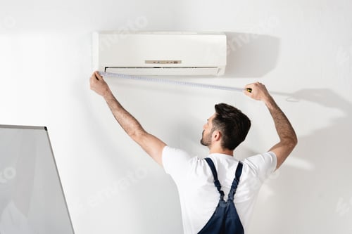 Preview: young repairman measuring air conditioner fixed on white wall in office