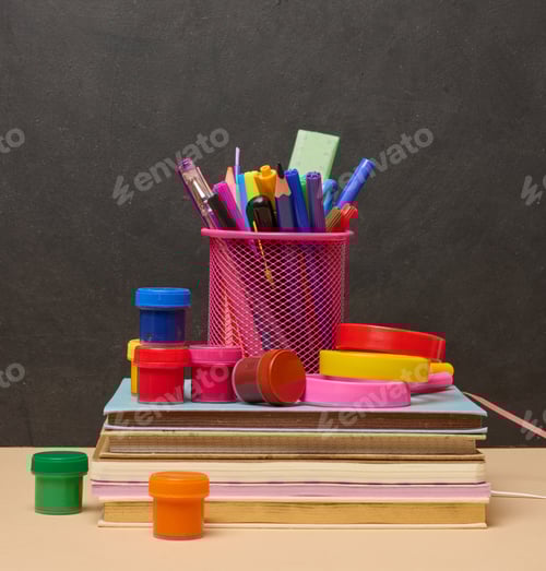 Visualização: Uma pilha de livros coloridos, um copo rosa com canetas e lápis e duas lupas