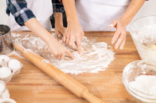 Preview: Hands of mother and son drawing on table with flour while going to knead dough