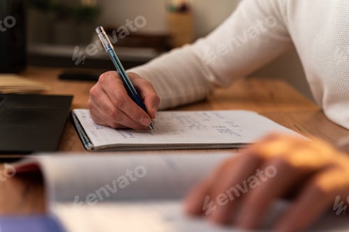 Preview: Cropped view of the caucasian man writing on the notebook of his day planner while working at laptop