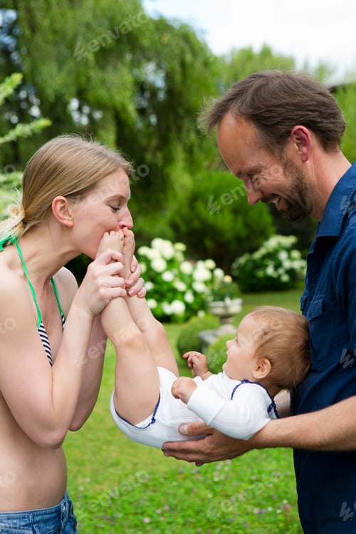 Preview: Mother kissing baby daughters feet in garden