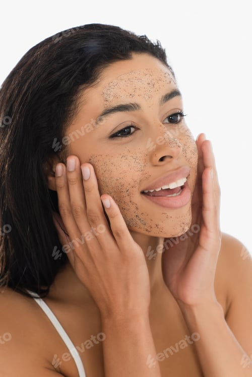 Preview: smiling young african american woman touching face with scrub isolated on white