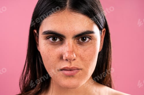 Preview: Young woman with freckles posing in studio with pink background