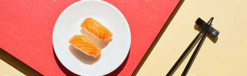 Preview: top view of fresh nigiri with salmon near chopsticks on red and beige surface, panoramic shot