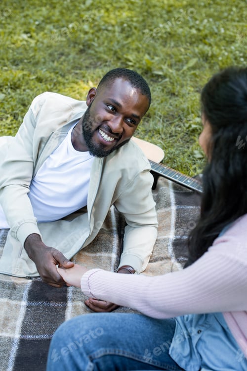 Preview: african american couple holding hands and looking at each other at picnic in park