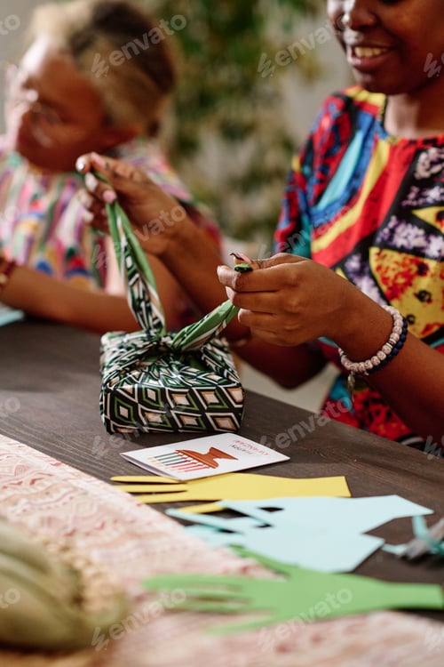 Preview: Hand of young African American woman tying knot on top of packed giftbox