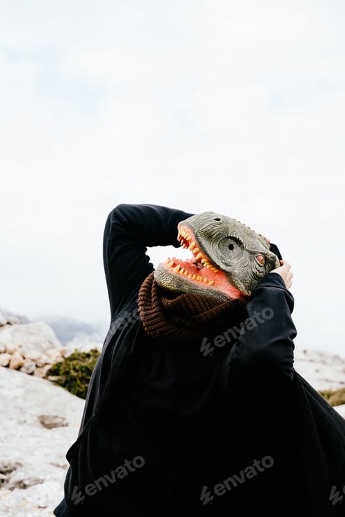 Preview: Caucasian man with a dinosaur mask and a cape surprised, shrieking and holding his hands to his head