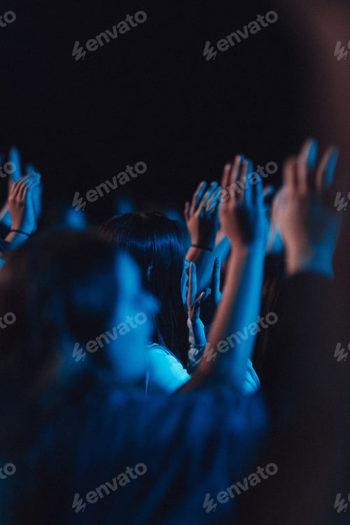 Preview: Vertical shot of believers in worship gathered in a hall with blue light effect