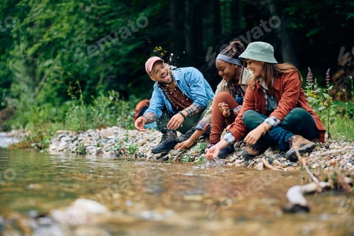 Preview: Happy hikers having fun while splashing water by mountain creek.