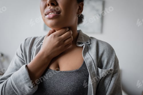 Preview: Cropped view of young multiracial woman touching sore throat at home