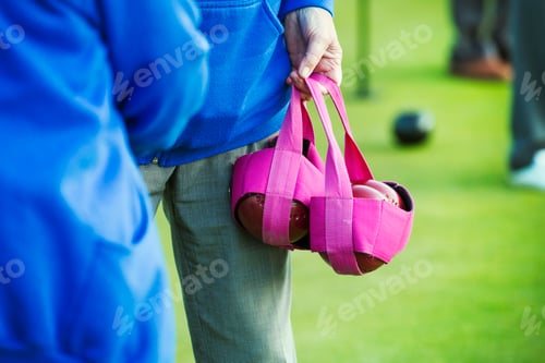 Preview: Two people in blue shirts, one carrying four wooden lawn bowls in a pink bag.