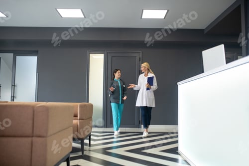 Visualização: Médico sênior e jovem estagiário compartilhando informações no corredor