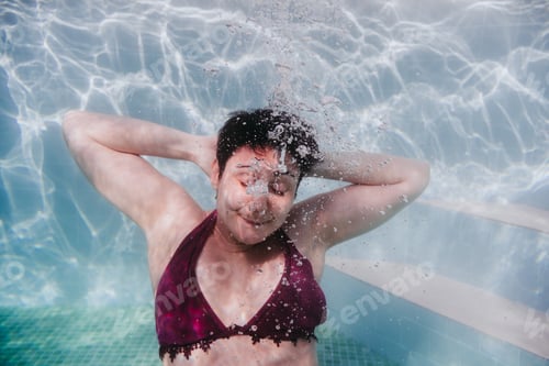Preview: young woman diving underwater in a pool. arms resting behind the head. summer and fun lifestyle