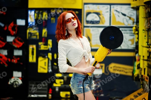 Preview: Red haired model posed with large angle grinder at store or household shop of working tools.