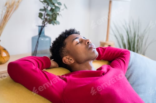 Preview: Dreamy black man sleeping on sofa at home with closed eyes