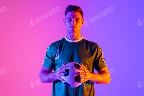 Preview: Portrait of caucasian male soccer player with football over neon pink lighting