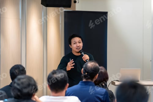 Preview: Asian Speaker with casual suit on the stage in front of the room with low light