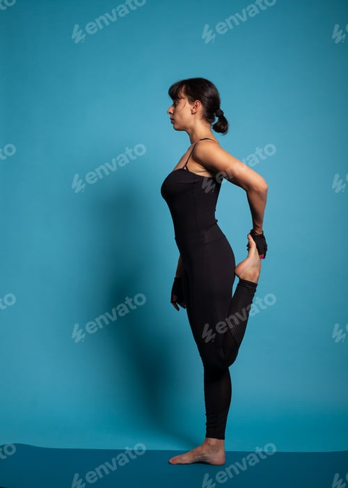 Preview: Caucasian female in sportswear standing on yoga mat stretching leg