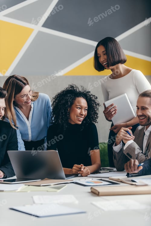 Preview: Happy young business team looking at laptop while having group meeting in the office together