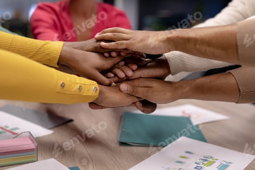 Preview: Cropped hands of biracial female and male colleagues stacking hands over conference table in office