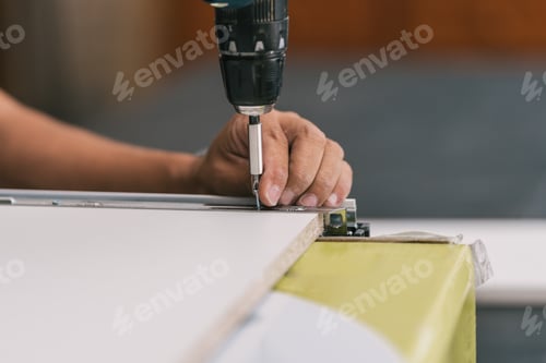 Preview: Detail of a man's hand holding a screw and a drill in a workshop