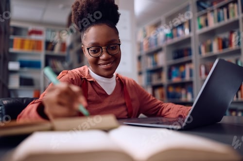 Preview: Happy black female student e-learning on laptop in library.